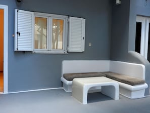 A room with a white bench, a white sofa, and a window with white shutters. - Tataki Family Hotel (Santorini)