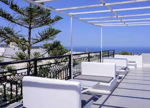 Un balcon doté de mobilier blanc, d’une rambarde en métal et offrant une vue sur la mer et les bâtiments.