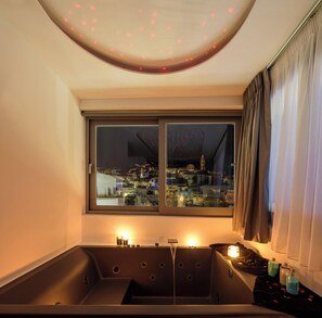 Ein modernes Badezimmer mit einer großen Badewanne, einem Fenster mit Stadtblick und einer Deckenleuchte.