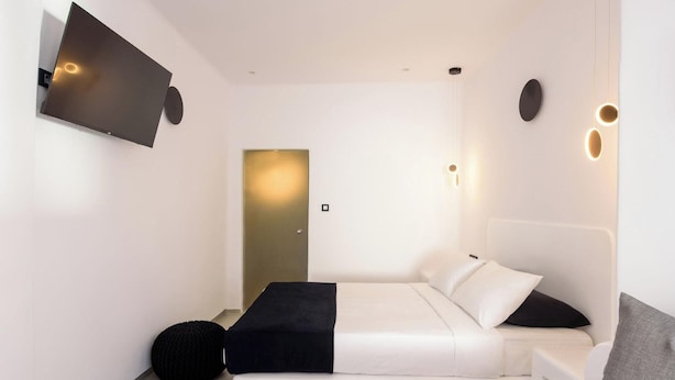 A modern bedroom with a bed, a bench, a wall-mounted TV, and a door. - Tataki Family Hotel (Santorini)