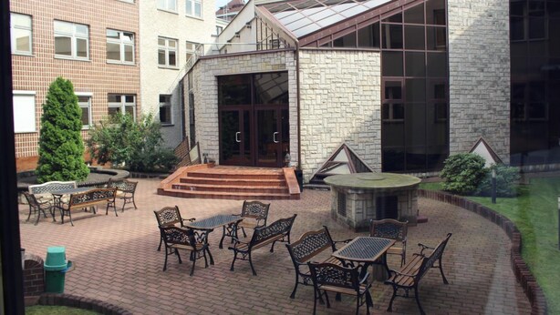 A courtyard with outdoor seating, a stone building with a glass entrance, and a brick wall. - Centrum Konferencyjne Ibib Pan (Warsaw)