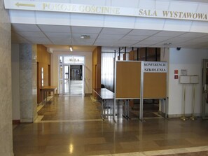 A corridor with a sign indicating a conference room and a direction sign pointing to a room labeled 'AULA'. - Centrum Konferencyjne Ibib Pan (Warsaw)