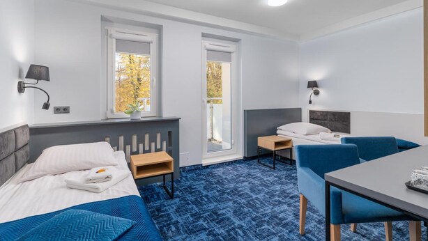 Quarto de hotel com duas camas, uma escrivaninha, uma cadeira e uma janela com vista para árvores de outono.