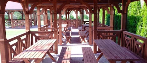 An outdoor wooden pavilion with picnic tables and benches, surrounded by greenery.