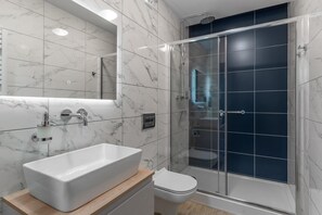Un baño moderno con tocador de mármol, lavamanos blanco, inodoro y cabina de ducha con paredes de vidrio.