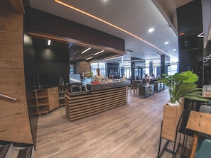 Un interior moderno con mostrador central, suelo de madera y zona de estar con mesas y sillas.