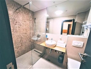 Un baño moderno con cabina de ducha de vidrio, un lavabo con espejo y un perchero para toallas.