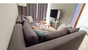 Ein modernes Wohnzimmer mit einer Couch, einem kleinen Tisch, einem Fernseher und einem Fenster mit Vorhängen.