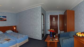 Habitación de hotel con dos camas, un escritorio con frutero, televisión y una puerta que da a otra habitación.