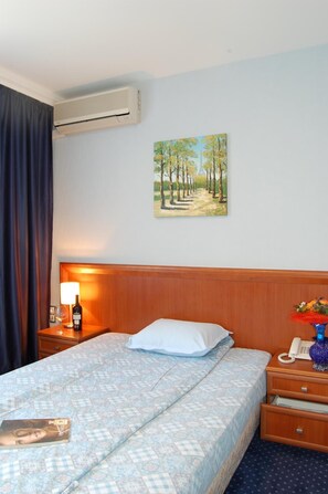 A hotel room with a bed, a nightstand, a lamp, a painting, and an air conditioning unit. - Hotel Kibella (Sofia)