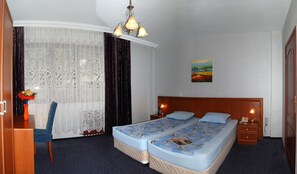 A hotel room with a bed, a desk, a chair, a desk lamp, a painting, and a window with curtains. - Hotel Kibella (Sofia)