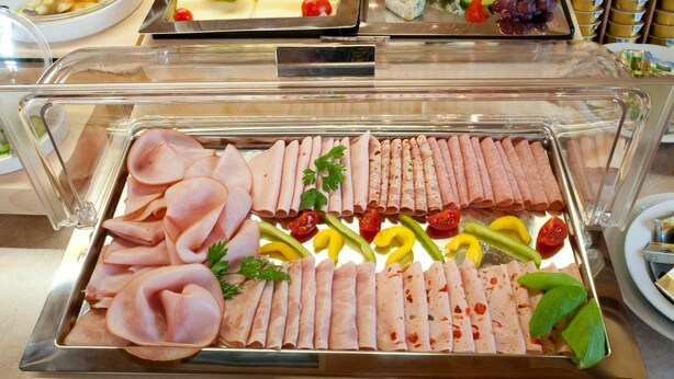 Un bufé con diversos alimentos, incluyendo carnes cortadas, quesos y vegetales.