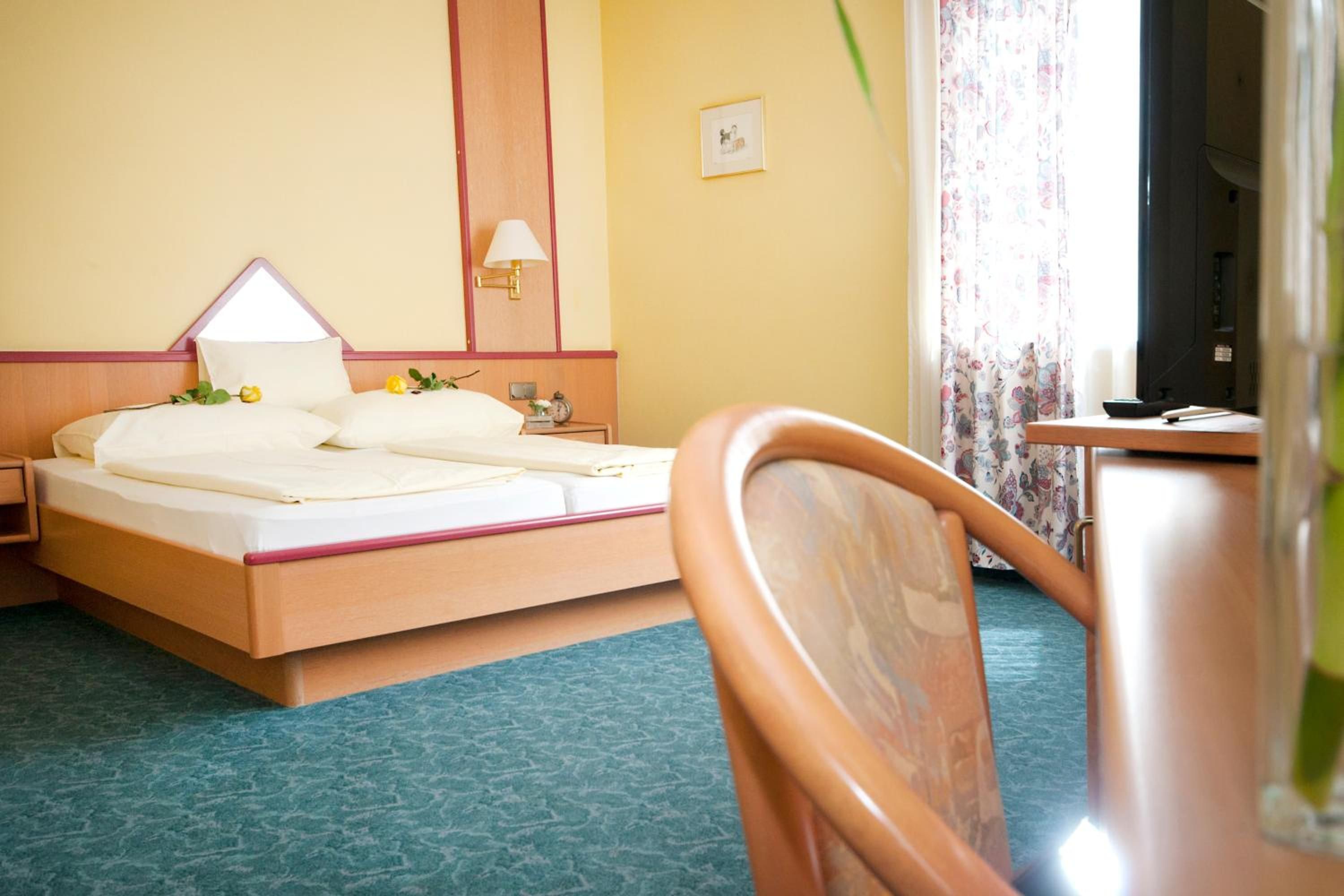 A hotel room with a bed, bedside table, lamp, and a view of the outside.