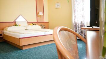 A hotel room with a bed, bedside table, lamp, and a view of the outside.