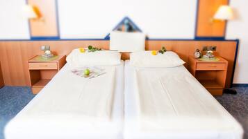 A hotel room with two single beds, a nightstand with a lamp, and a wall-mounted clock.