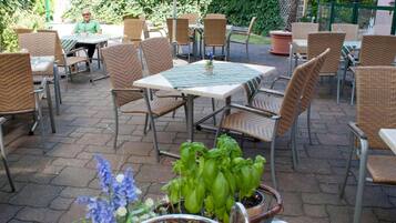 An outdoor patio area with wicker chairs and tables, some with striped tablecloths.