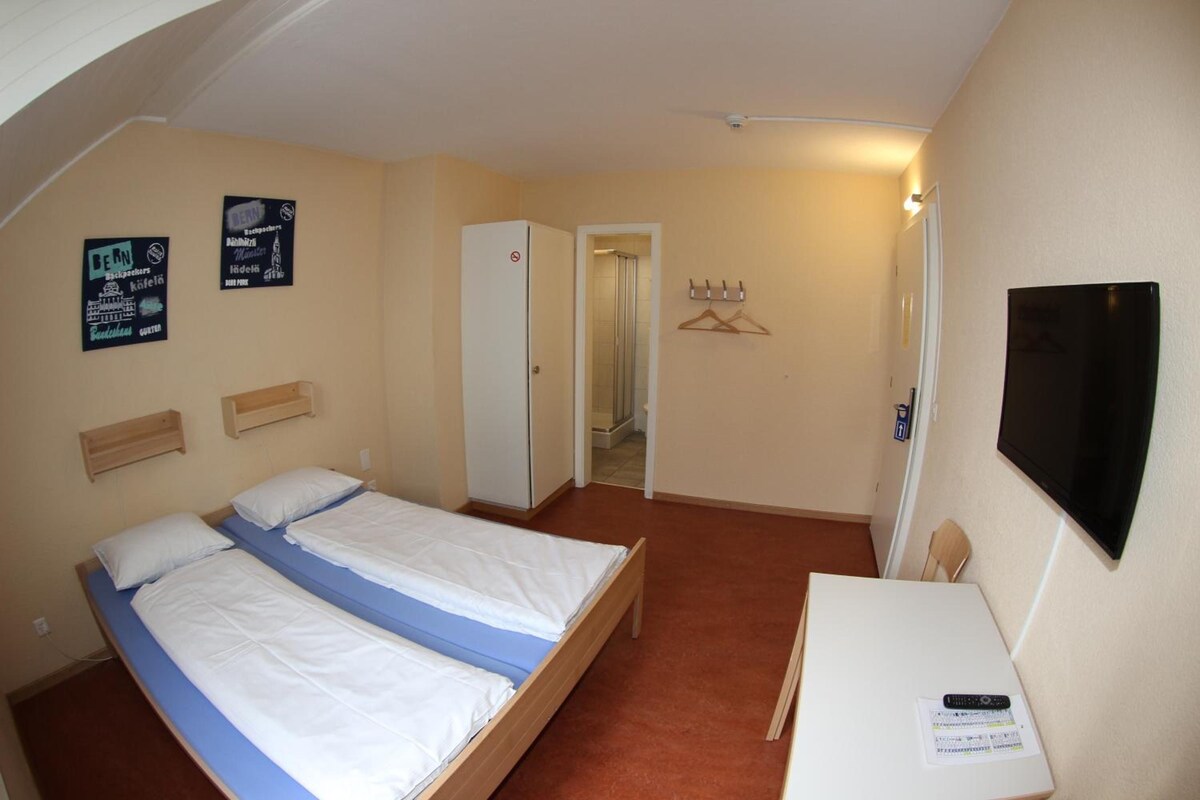A hotel room with a bed, a desk, a television, and a door leading to a bathroom.