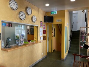 A reception area with multiple clocks, a TV, and a staircase leading to another floor. - Bern Backpackers Hotel Glocke (Bern)