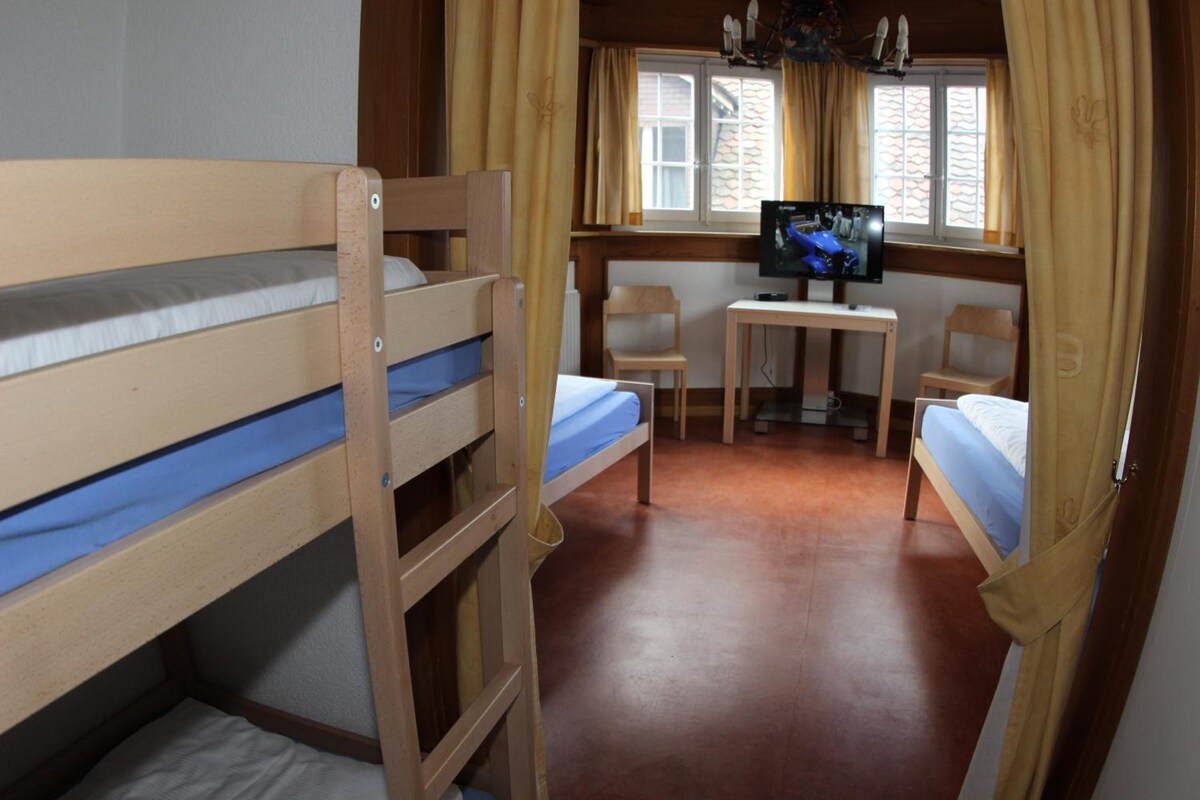A room with bunk beds, a desk, two chairs, and a television.