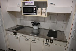 A kitchenette with a microwave, salt and sugar containers, and labeled drawers for pans, colanders, and big bowls. - Bern Backpackers Hotel Glocke (Bern)