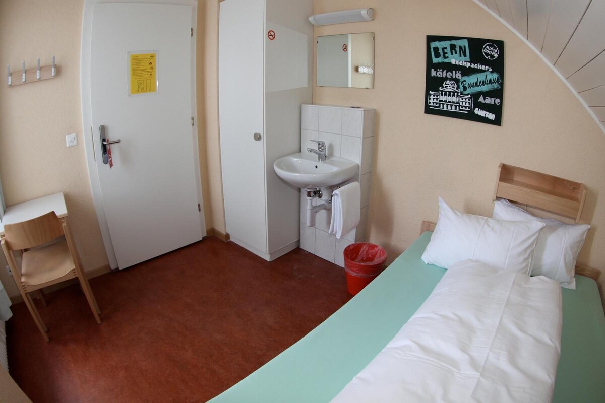 A hotel room with a bed, a chair, a sink, and a mirror.
