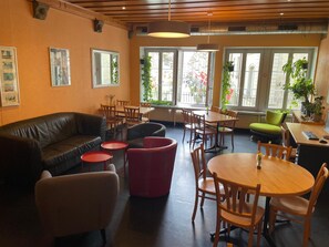 A modern interior with a leather sofa, red chairs, wooden tables, and large windows. - Bern Backpackers Hotel Glocke (Bern)