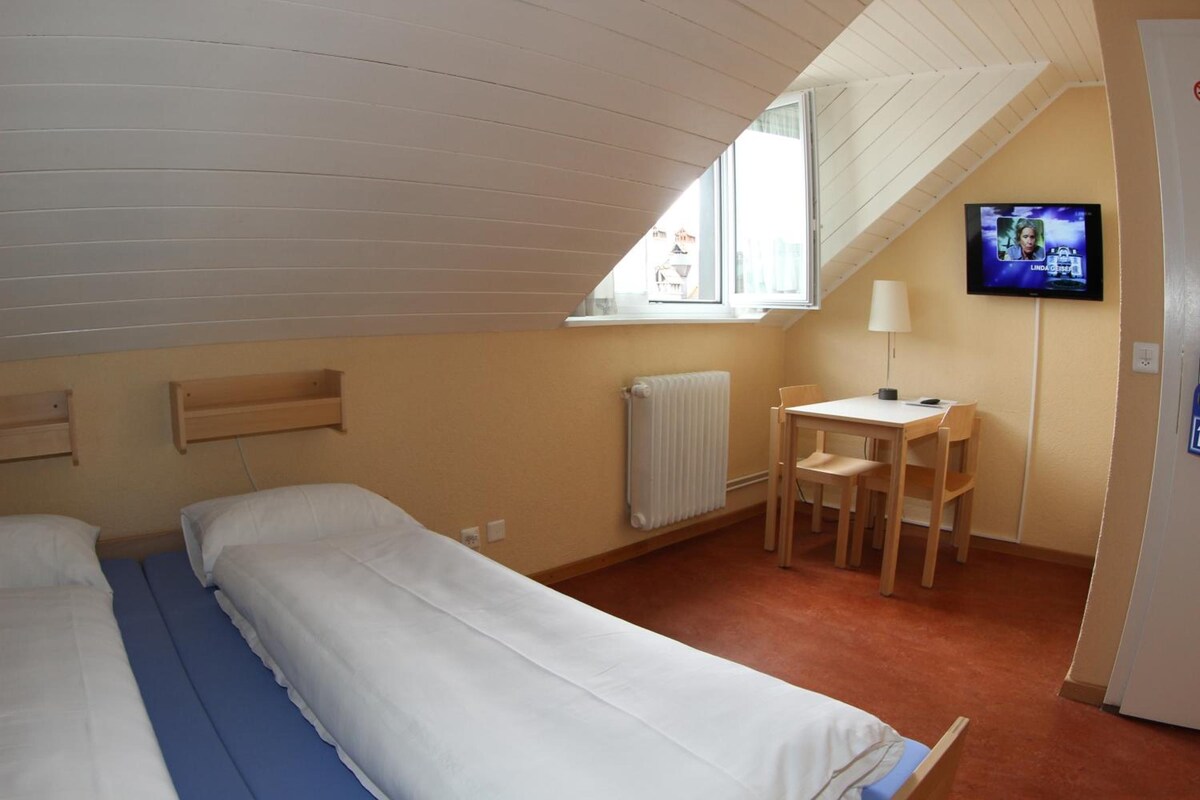 A room with two beds, a table with chairs, a TV, and a window.