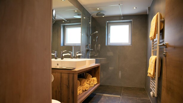 A modern bathroom with a wooden vanity, a toilet, a shower area, and a towel rack. - Weisses Lamm (Hallstatt)