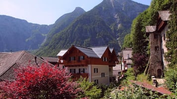 Ein Bergdorf mit traditionellen Holzhäusern, einem Steinhaus und einem Baum mit roten Blättern im Vordergrund.