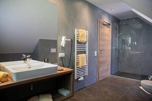 A modern bathroom with a large sink, towel racks, a glass shower enclosure, and a wooden vanity. - Weisses Lamm (Hallstatt)