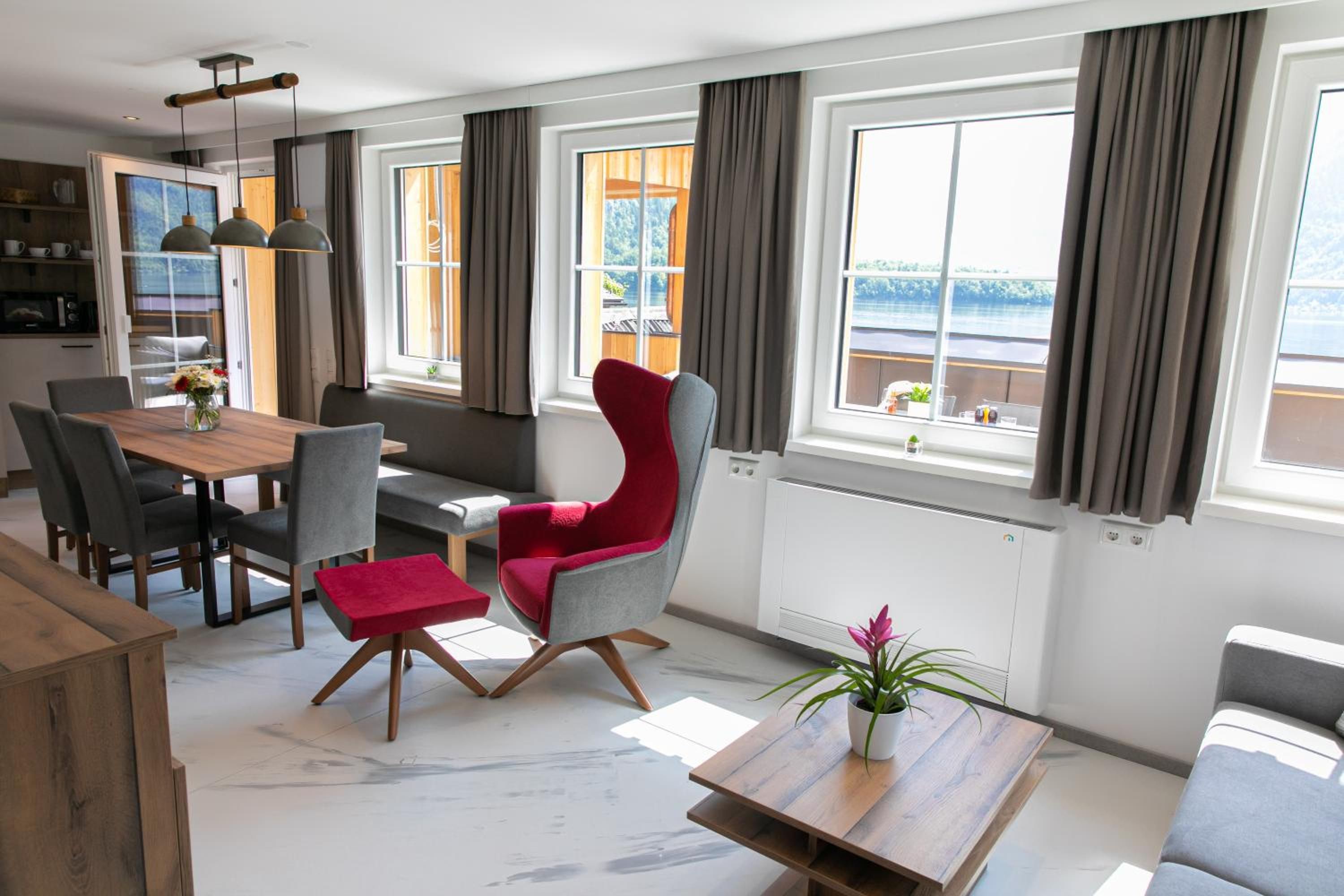 A modern living room with a dining area, large windows with curtains, and a view of the outdoors.