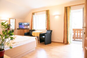 A hotel room with a bed, a desk with a TV, a chair, a small table, and a balcony with curtains. - Weisses Lamm (Hallstatt)