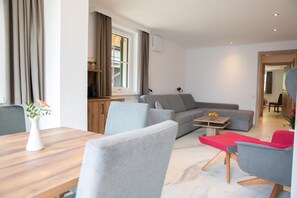 A modern living room with a sofa, chairs, a coffee table, and a dining area with a table and chairs. - Weisses Lamm (Hallstatt)
