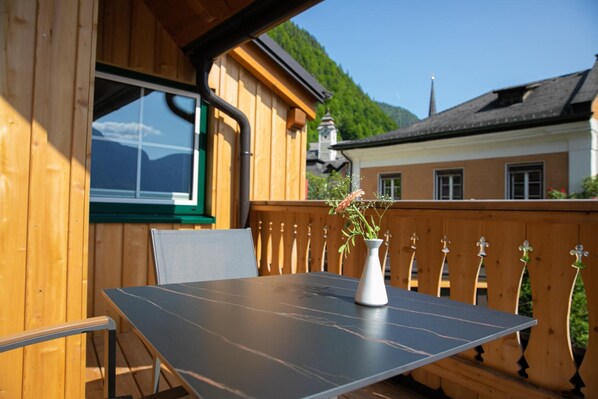 A wooden deck with a table and chairs, a window, and a view of a mountain and buildings. - Weisses Lamm (Hallstatt)