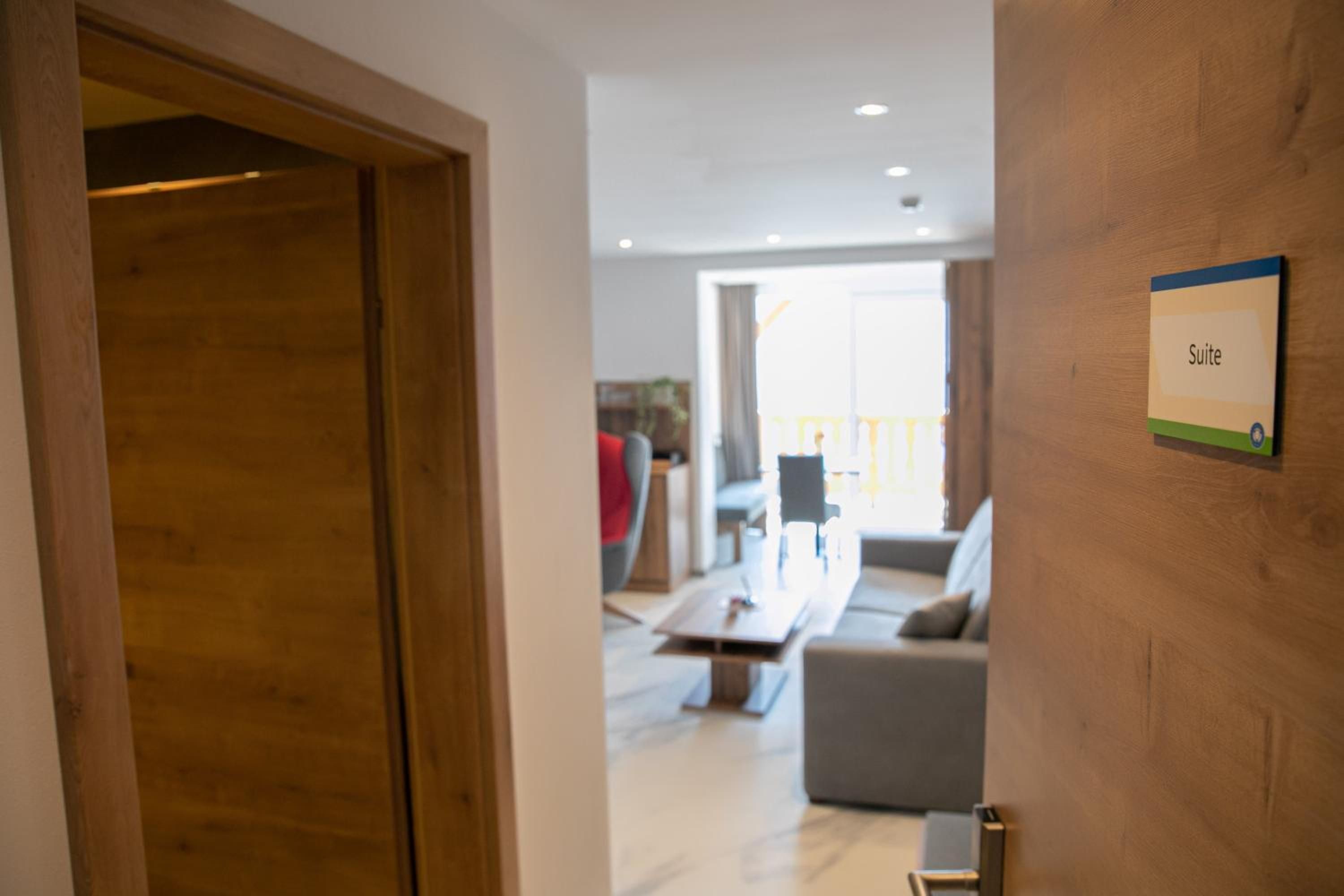 Habitación de hotel con puerta de madera, señal que indica la suite, un sofá, una mesa de centro y vistas al exterior.