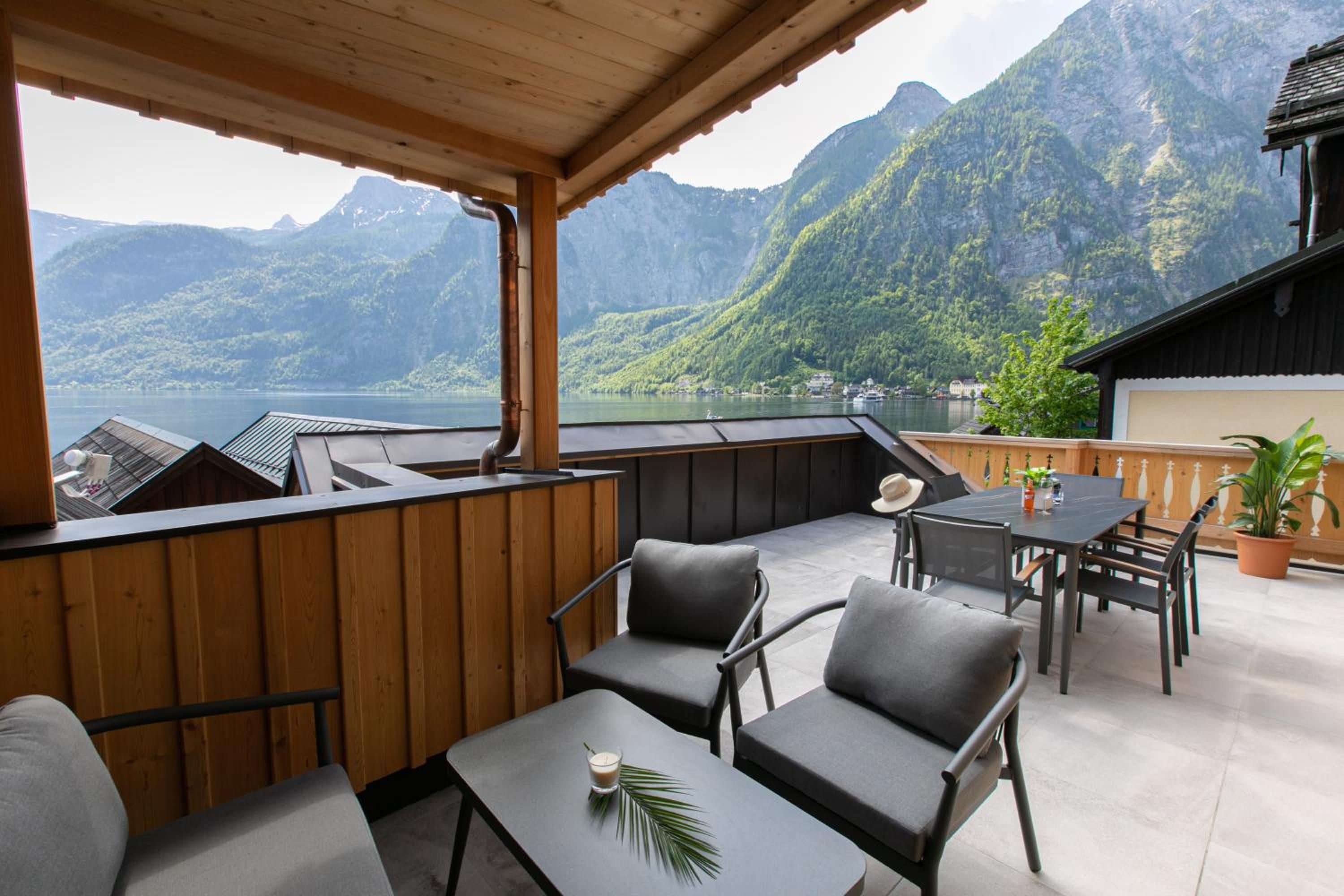 An outdoor patio with wooden furniture, a table, and a view of a lake and mountains.