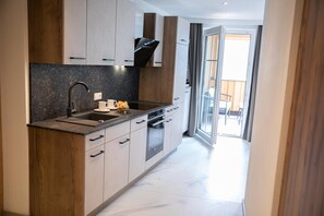 A modern kitchen with a built-in oven, a sink, and a window overlooking a balcony. - Weisses Lamm (Hallstatt)
