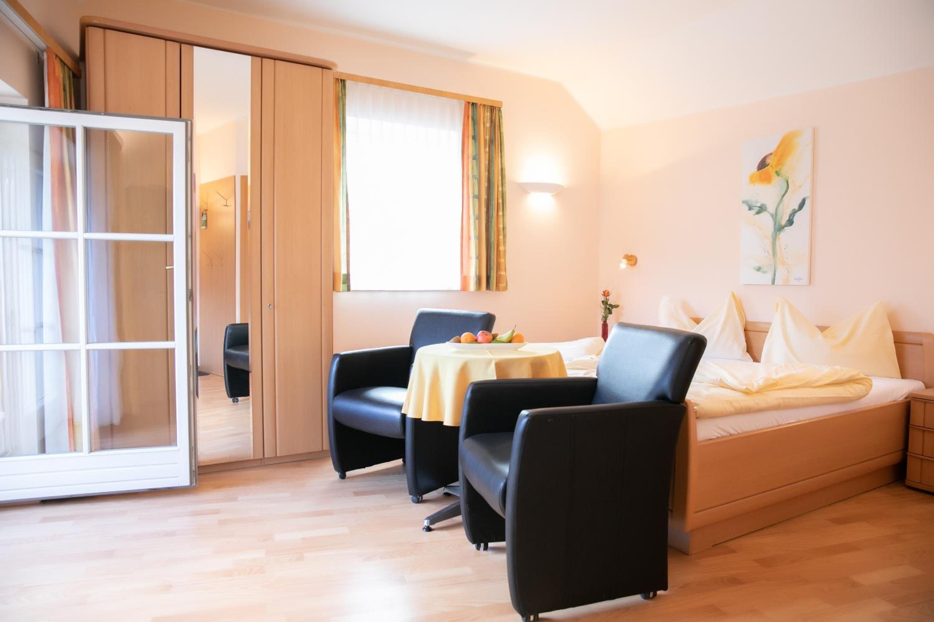 A hotel room with a bed, two chairs, a table with fruit, a painting, and a sliding door.