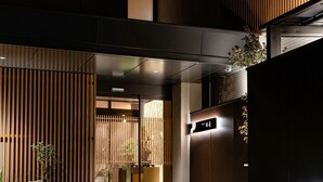 A modern building entrance with a wooden facade, a sign with Japanese characters, and a small potted plant. - Shikinoirodori Hatago (Kobe)
