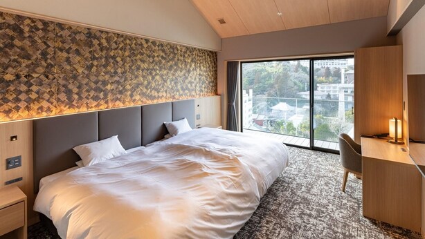A modern hotel room with a large bed, a desk, and a view of buildings through a large window. - Shikinoirodori Hatago (Kobe)