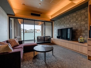 A modern living room with a sofa, a round table, a TV, and a view of the outdoors. - Shikinoirodori Hatago (Kobe)