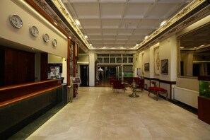 Un vestíbulo de hotel con recepción, relojes y una zona de estar con sillas y mesas.