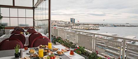 A dining area with a table set for breakfast, overlooking a waterfront with boats and buildings.