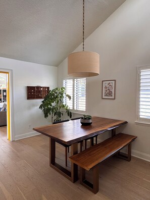 A dining area with a wooden table, bench, hanging light fixture, potted plant, and artwork. - Spacious, family-friendly beach house (Atlantic Beach)
