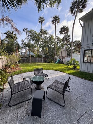 A patio with four chairs and a table, surrounded by a fence and palm trees. - Spacious, family-friendly beach house (Atlantic Beach)