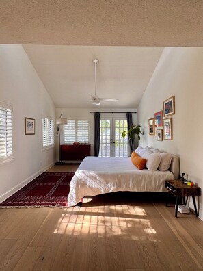 A bedroom with a bed, a nightstand, a red rug, a ceiling fan, and a view through a door. - Spacious, family-friendly beach house (Atlantic Beach)