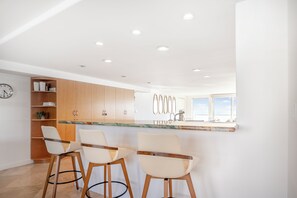 Eine moderne Küche mit Holzausstattung, einer Marmorarbeitsplatte und drei Barhocker.