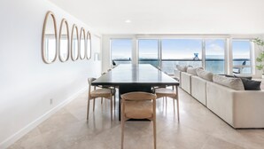 Un intérieur moderne comprenant une table à manger, des chaises, un canapé et de grandes fenêtres donnant sur la mer.