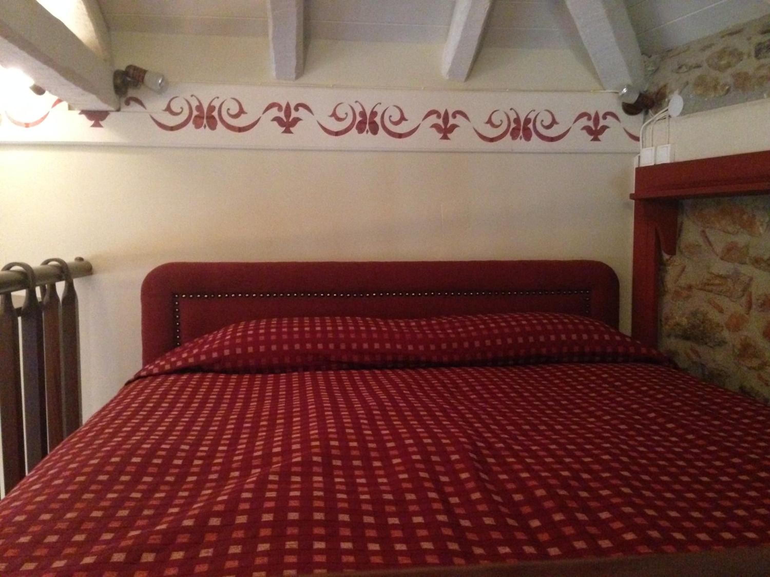 A bed with a checkered red and white bedspread, a wooden headboard, and a stone wall to the right.