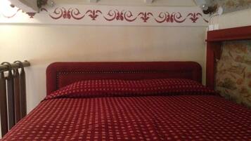 A bed with a checkered red and white bedspread, a wooden headboard, and a stone wall to the right.